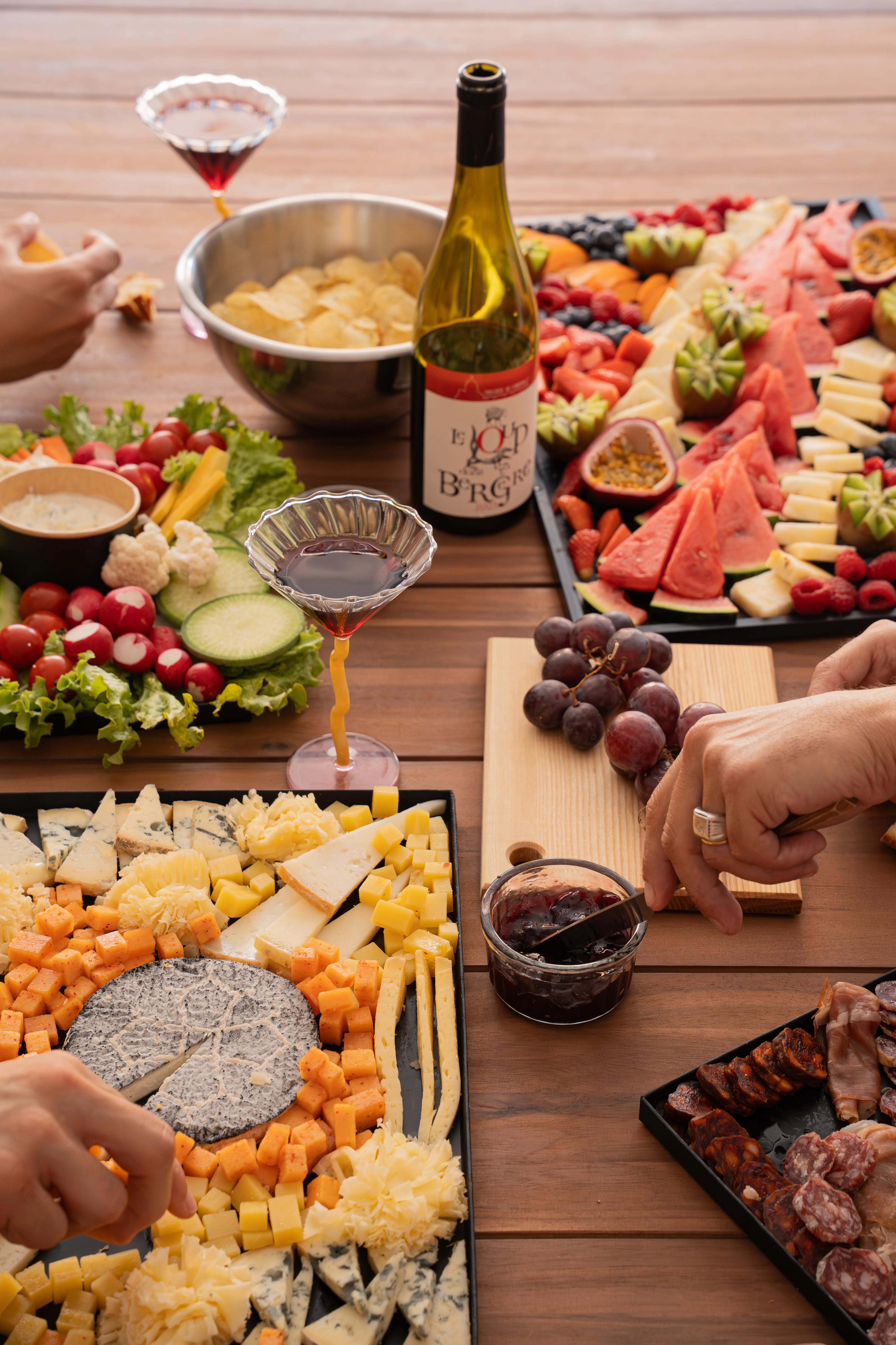 Table d'apéro garnie de planches de fromages, charcuteries et fruits frais avec une bouteille de vin